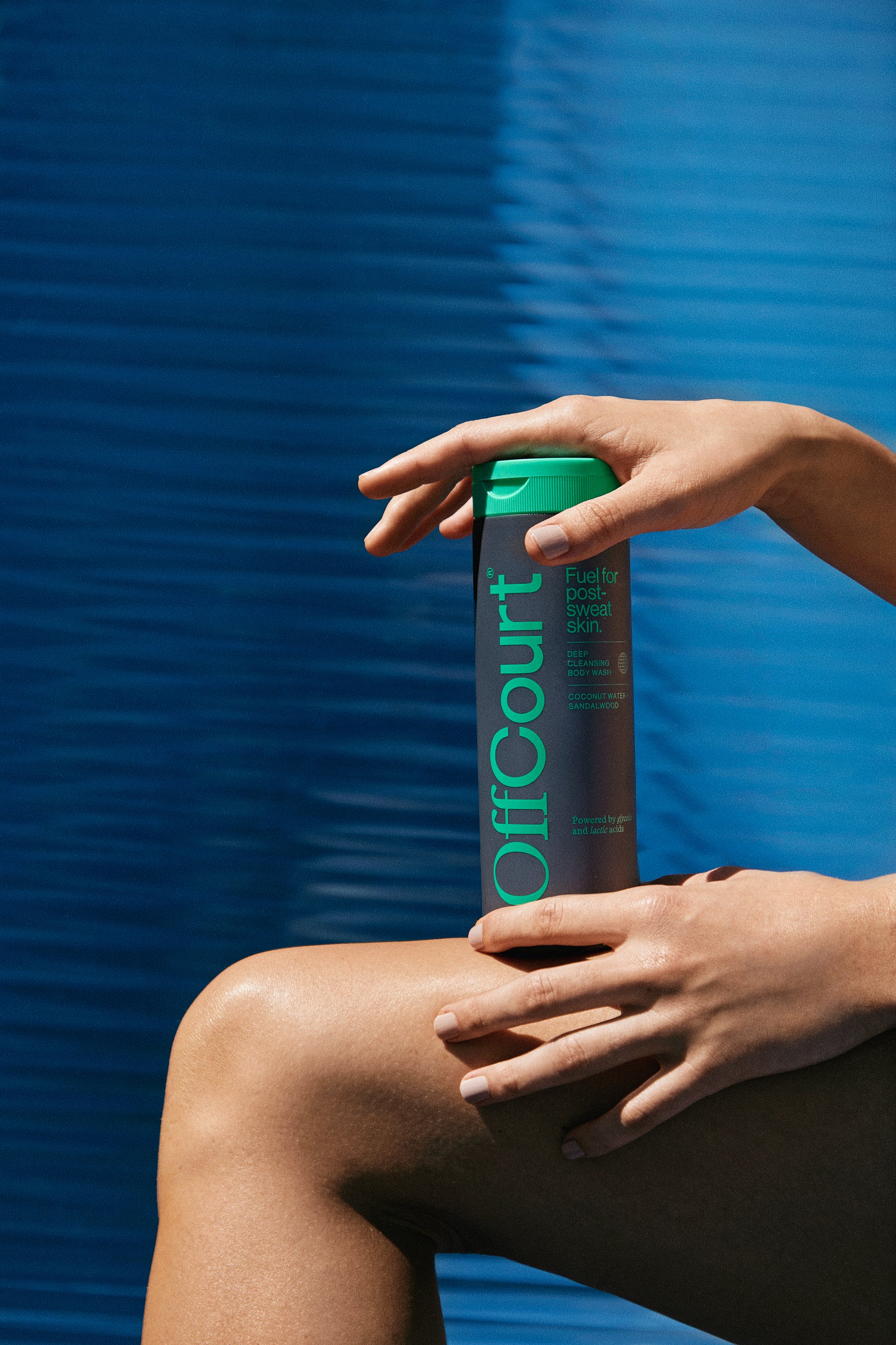 A woman holding a bottle of Deep Cleansing Body wash in coconut water + sandalwood